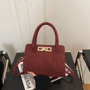 Burgundy matte leather trapezoid handbag with gold rotating clasp on fashion magazine