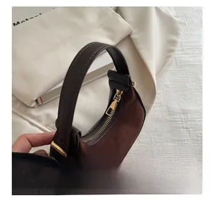 Detail of brown suede crescent bag featuring dark leather handle and golden metal zipper