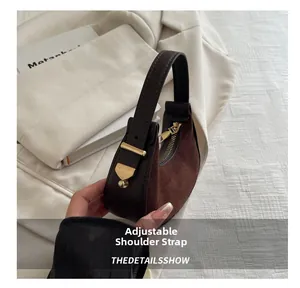 Detail of adjustable leather strap and gold hardware on dark brown suede crescent bag