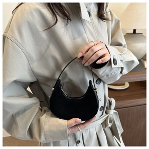 Detail view of mini black suede crescent bag with gold accents held by model