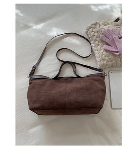 Vista piatta di una borsa tote in pelle scamosciata marrone scuro con maglione e gadget