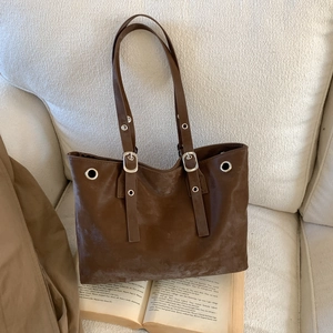 Brown faux suede tote bag with silver metal eyelets on a cozy cream sofa background
