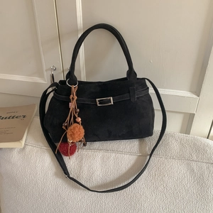 Black faux suede tote bag with vintage plush ball charm shown in a cozy indoor setting