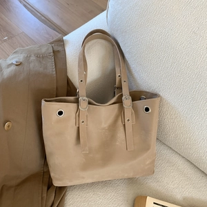 Retro khaki leather tote bag with silver eyelets and adjustable strap on white sofa