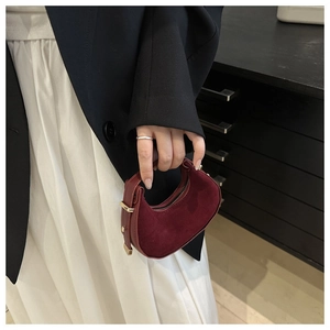 Detail of burgundy crescent mini bag in suede and smooth leather held by a model