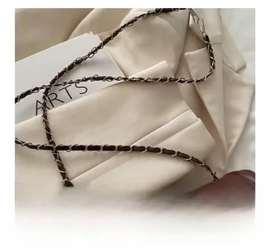 Detail of the woven metal chain strap and brown quilted leather texture of the bag