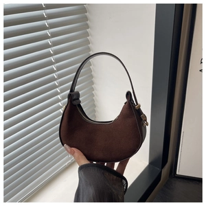 Close-up of brown suede crescent bag with smooth leather handle and gold zipper detail