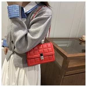 Detail of red quilted leather handbag with gold twist lock and metal chain strap on model