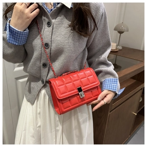 Detail of red quilted faux leather handbag featuring a silver chain strap and metal lock