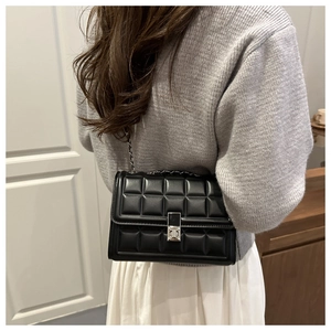 Rear view of a model wearing a black quilted leather shoulder bag with silver chain strap