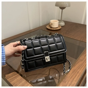 Detail of black quilted bag with silver swivel lock and chain strap on a wooden table