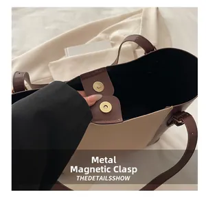 Detailed close-up of the magnetic gold clasp on a two-tone leather tote bag