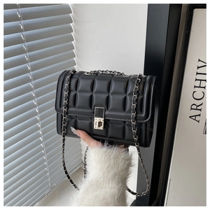 Detail of black quilted crossbody bag with silver chain strap and metallic twist lock