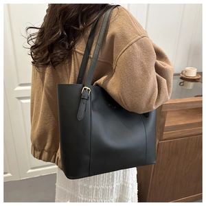 Detail of minimalist black tote bag with gold buckle and adjustable strap on a model