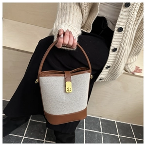 Detail of cream canvas bucket bag with brown leather trim and golden twist lock closure