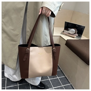 Detail of a large two-tone leather tote bag featuring a gold brand logo and adjustable straps