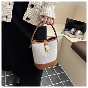 Chic beige canvas bucket bag with brown leather trim held by a model in a warm setting