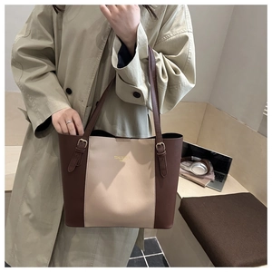 Detail of a brown and beige two-tone tote bag with gold logo and adjustable strap