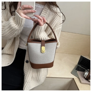 Detail of a brown leather and beige canvas bucket bag held by a woman in a casual setting