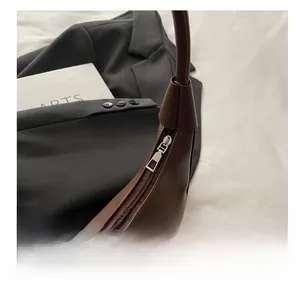 Close-up of a smooth silver metal zipper on a brown leather crescent shoulder bag