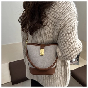 Detail of canvas bucket bag with brown leather trim and gold metal lock on a model