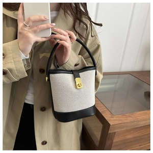 Detail of canvas and leather bucket bag featuring a gold metal twist lock and stitching