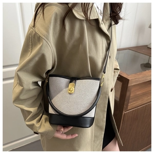 Detail of crossbody bucket bag in cream fabric and black leather on trench coat