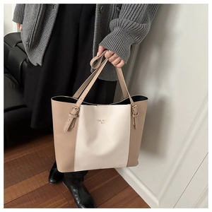 Detail of large beige and tan tote bag with brand lettering held by model in casual outfit