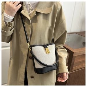Close-up of contrast stitching on beige and black bucket bag with gold clasp detail