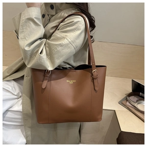 Brown faux leather tote bag with gold hardware worn over the shoulder by a model
