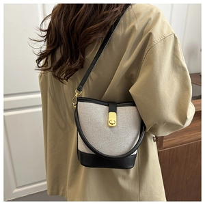 Detail of canvas bucket bag with black leather trim and golden metal turn-lock closure