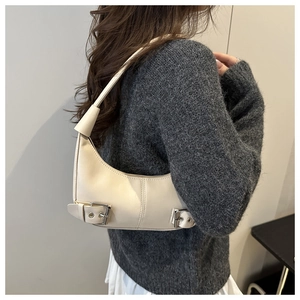Detail of a beige crescent hobo bag with silver buckle straps worn on the shoulder