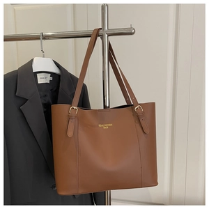 Close-up of caramel leather tote bag with gold logo and adjustable shoulder straps