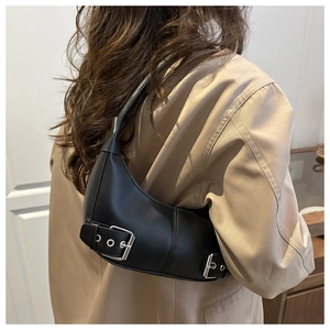 Detail of a black crescent moon shoulder bag with silver eyelet straps on a trench coat