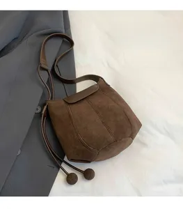 Detail of dark brown suede bucket bag with drawstring closure over a grey blazer