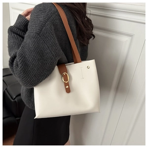 Détail d'un sac cabas crème avec des lanières brunes et une boucle dorée sur le côté