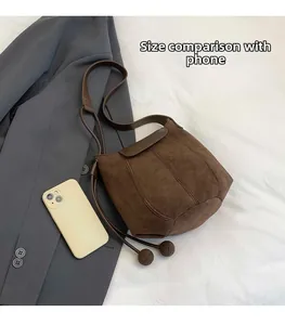 Deep brown suede bucket bag size comparison with a smartphone on grey fabric