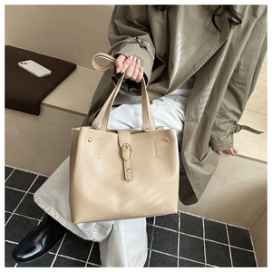 Détail d'un sac cabas beige avec boucle dorée et lanière sur un banc en bois