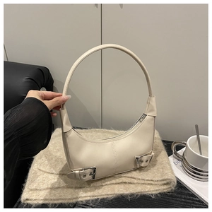 Detail of off-white crescent bag with silver buckles on soft fabric background