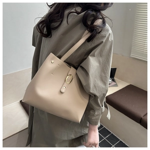 Sac fourre-tout beige chic avec boucle dorée porté par un mannequin dans un décor