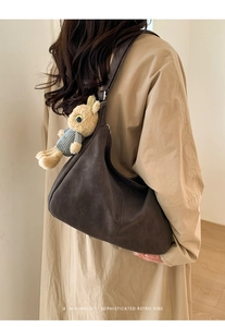 Detail of retro dark brown suede tote bag with cute rabbit plush keychain on shoulder strap