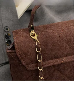 Close-up of golden metal lobster clasp and chain on dark brown quilted handbag