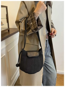 Detail of black suede bucket bag featuring vertical stitching and a small round charm