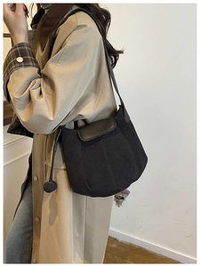 Detail of a black matte bucket bag with spherical drawstring tassel on a trench coat