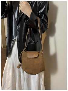 Detail of brown suede bucket bag with leather flap and spherical drawstring on a model