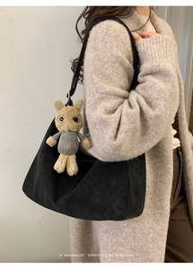Detailed view of black matte underarm bag with cute plush pendant on a soft knit sweater