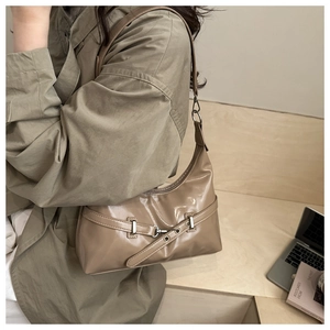 Detailed side view of khaki patent leather underarm bag with decorative metal buckles