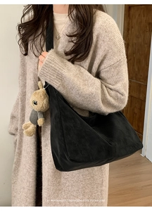 Detail of black suede hobo bag with a plush brown rabbit pendant on a beige cardigan