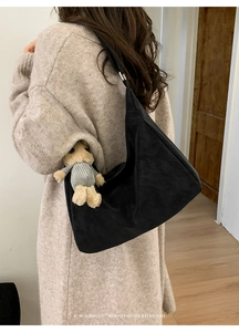 Close-up of matte black minimalist underarm bag with wide strap on a beige sweater