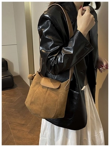 Brown frosted suede bucket bag with leather flap shown on a model in a minimal interior